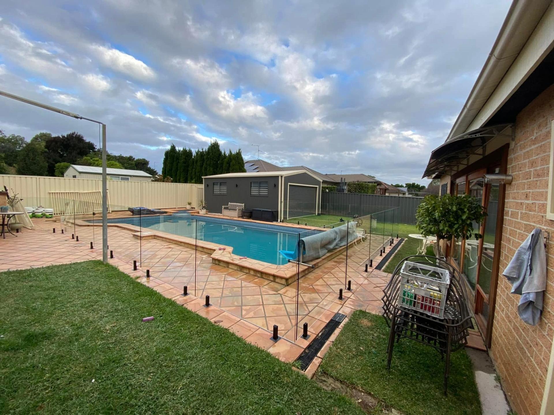 Frameless glass pool fence around a backyard pool